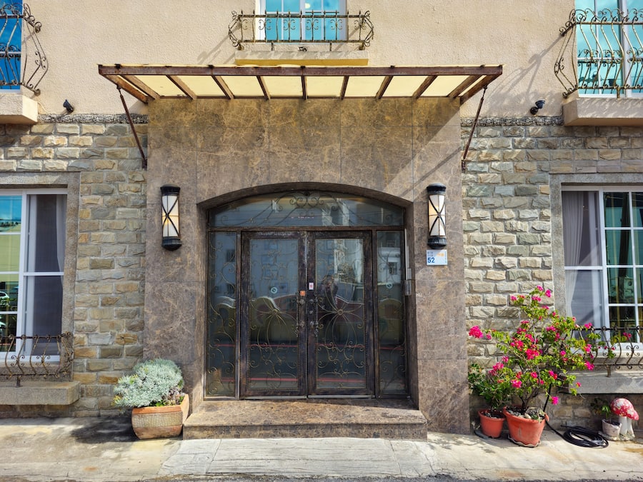 Un edificio de piedra con una entrada arqueada grande, plantas en macetas y un balcón con barandillas de metal.