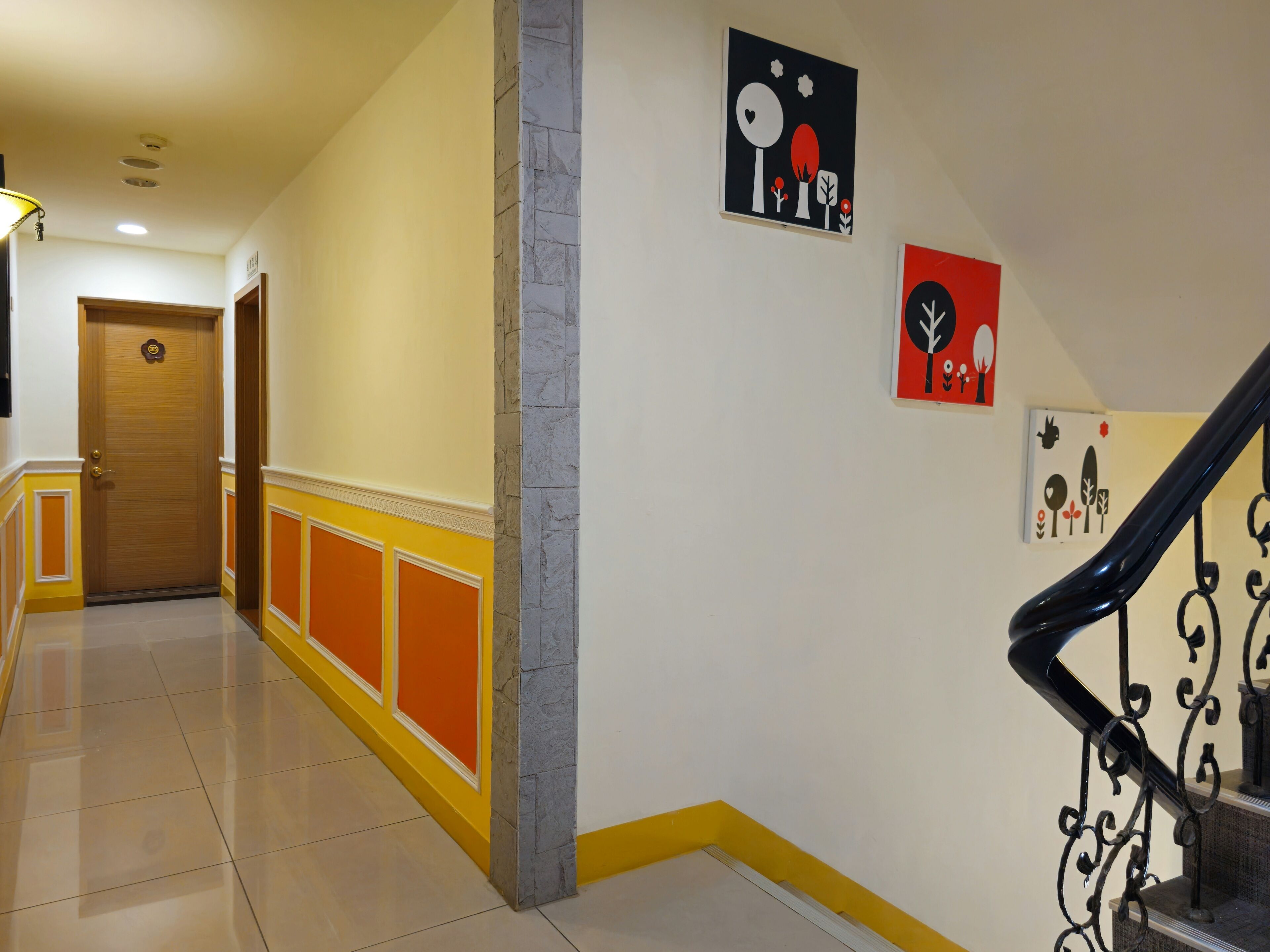 A hallway with a wooden door, a staircase with a black handrail, and two wall-mounted artworks.