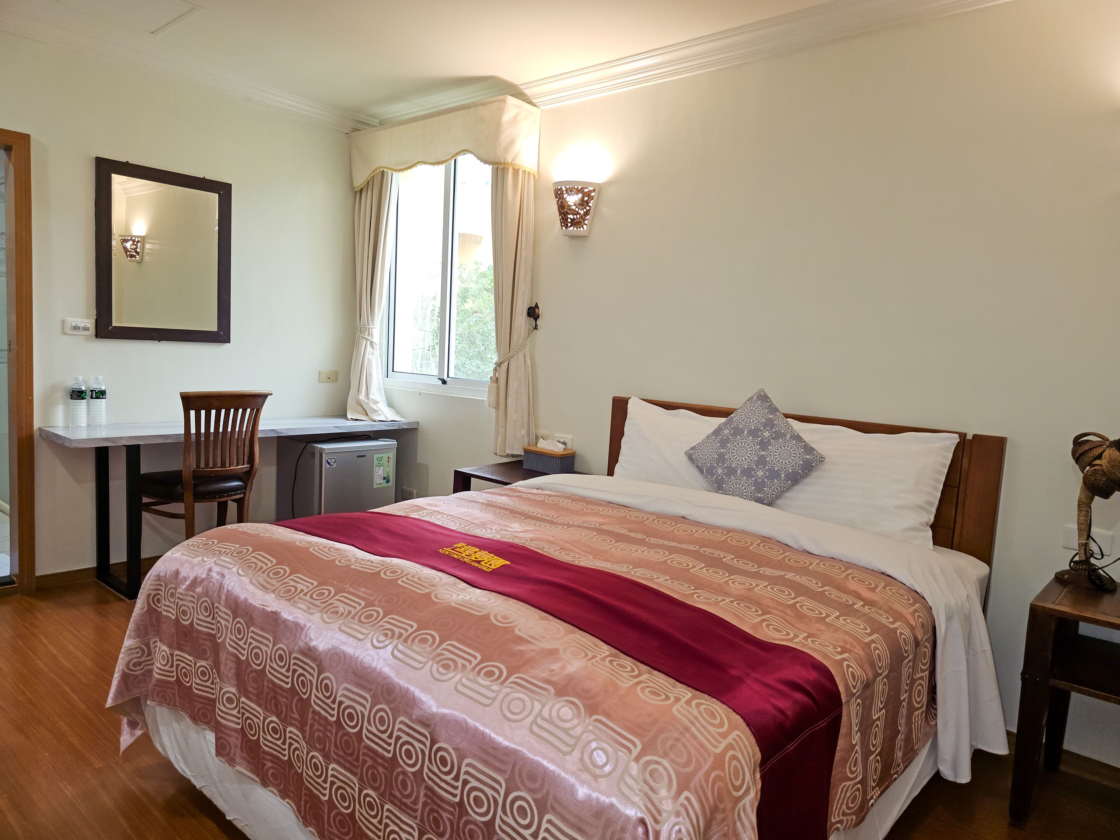 Una habitación de hotel con cama, escritorio, silla, mesita y mesita de noche.