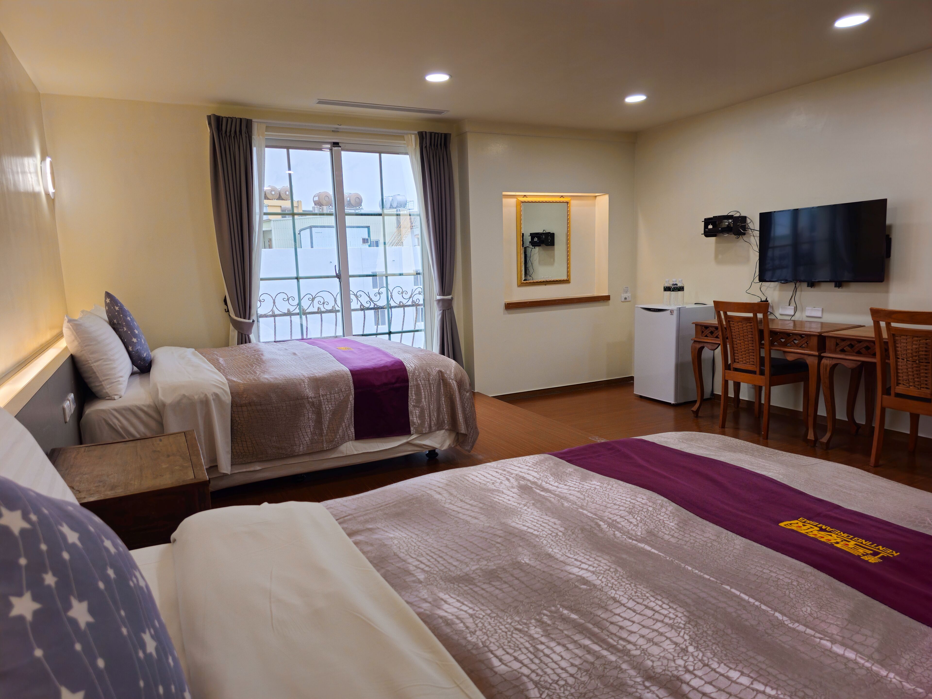 A hotel room with two beds, a desk with a TV, and a balcony with a view.