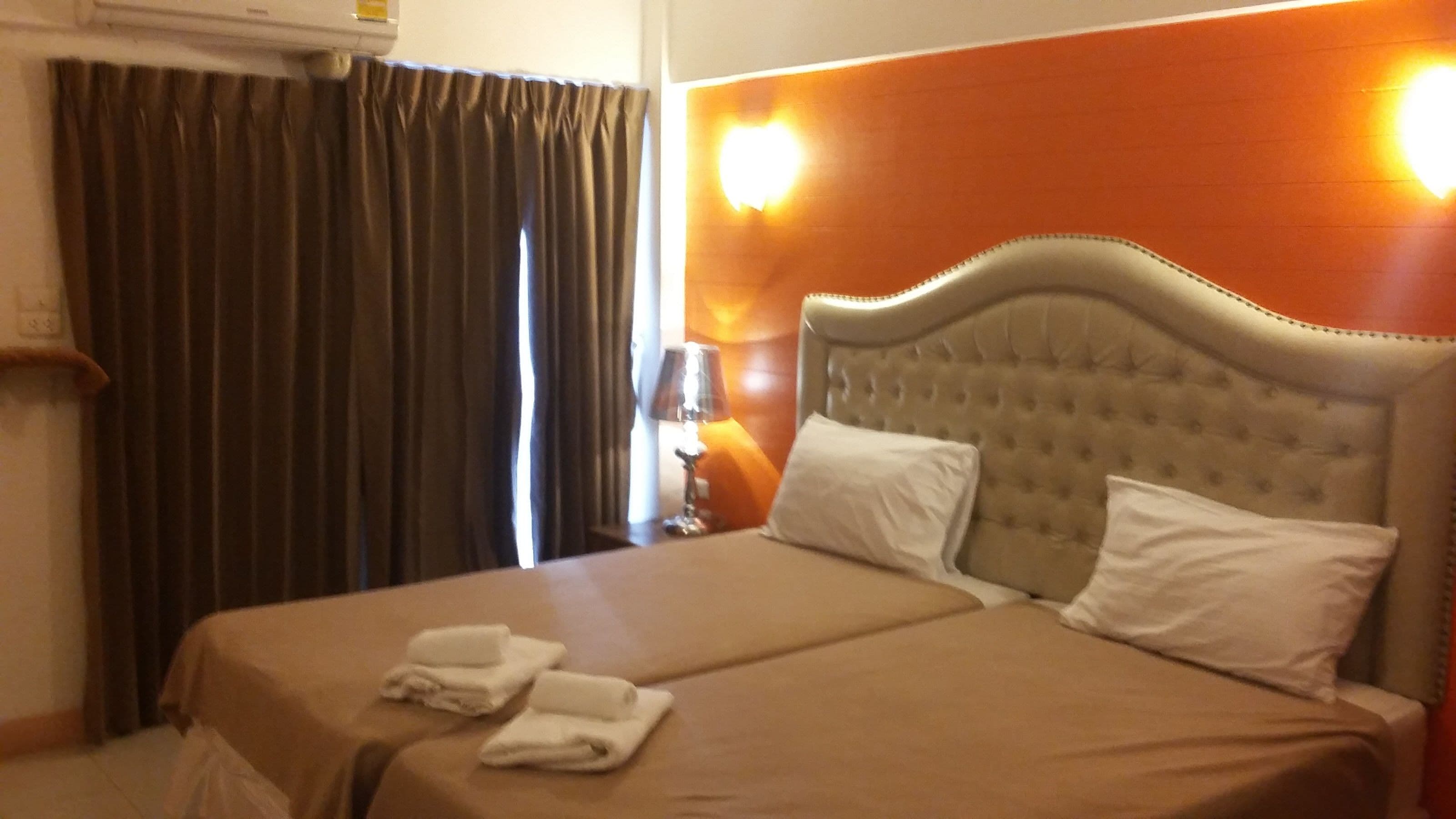A hotel room with a large bed, two pillows, a lamp, and a window with curtains.