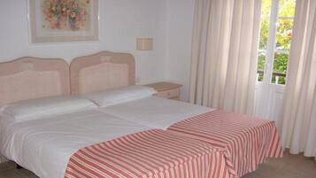 Ein Doppelbett mit weiß-rot gestreifter Bettdecke, ein Nachttisch, eine Wandlampe und ein Fenster mit Vorhängen.