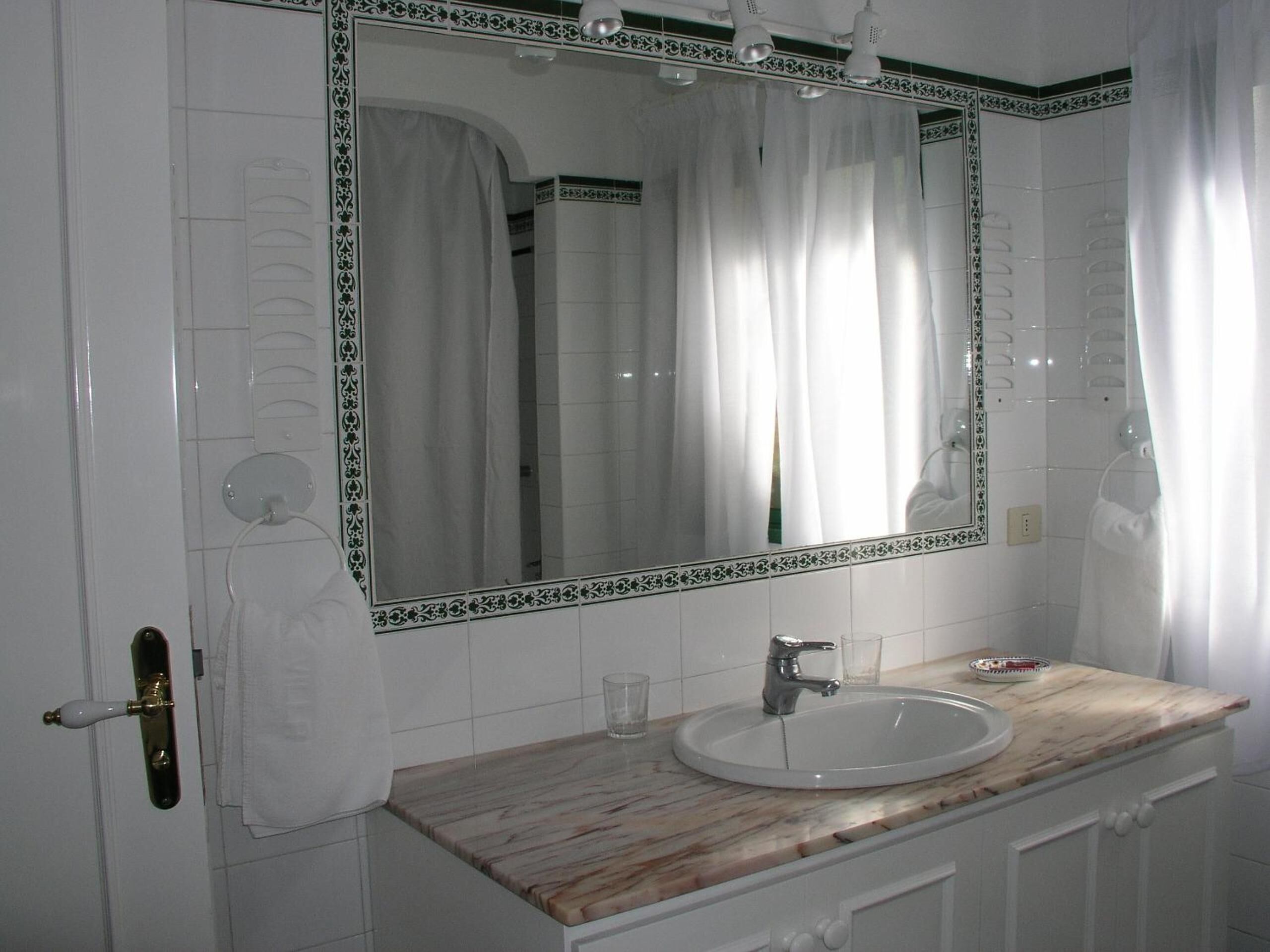Un baño con lavamanos de mármol, un espejo grande con marco decorativo y azulejos blancos.