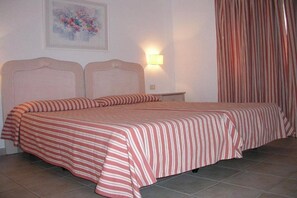 A double bed with striped bedding, a nightstand, a wall-mounted lamp, and a floral painting.