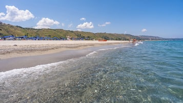 Una spiaggia con acque cristalline, una costa sabbiosa e un paesaggio collinare sullo sfondo.