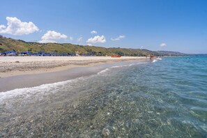 A beach with clear water, a sandy shore, and a hilly landscape in the background. - Le Dune Beach Club (Messina)
