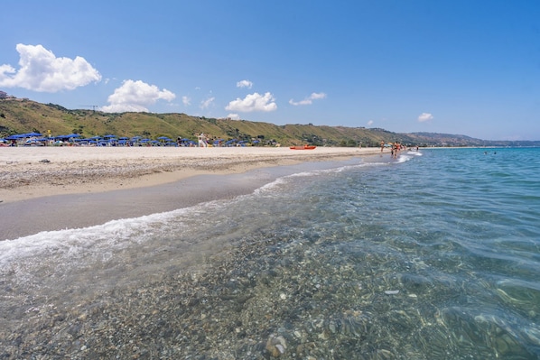A beach with clear water, a sandy shore, and a hilly landscape in the background. - Le Dune Beach Club (Messina)