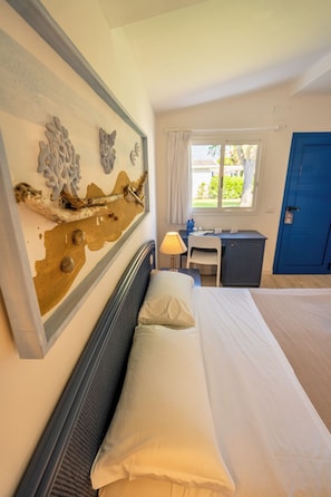 Une chambre d’hôtel avec un lit, un bureau, une chaise, une fenêtre et une porte bleue.