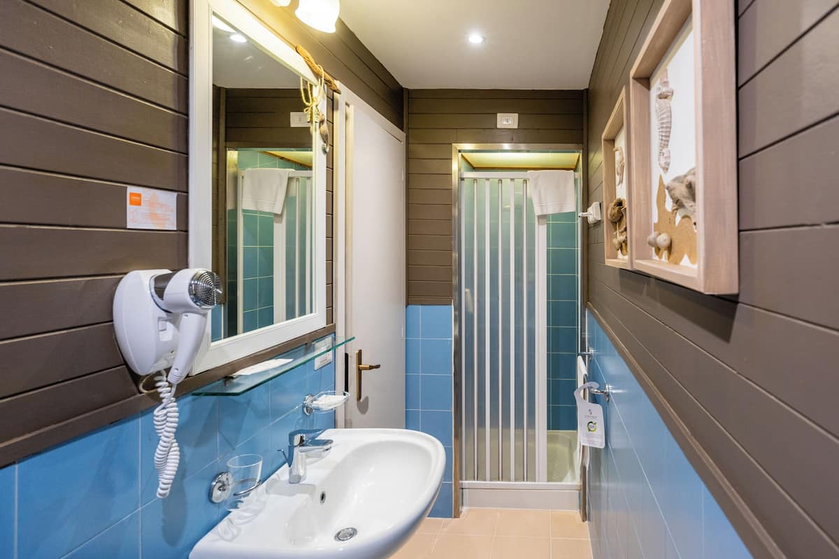 A bathroom with a white sink, a hairdryer, a glass shower enclosure, and a mirror with lights.