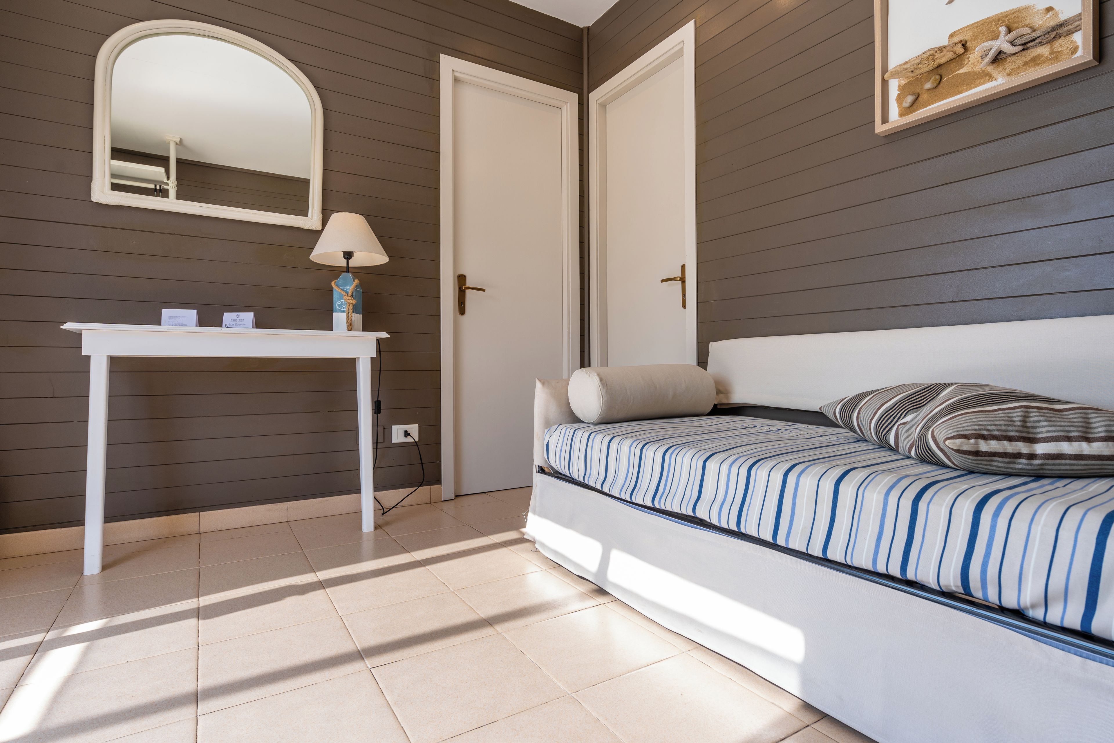 Una camera da letto con un letto, un comodino, una lampada, uno specchio e una porta.