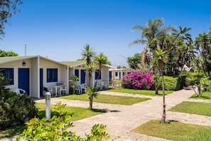 A hotel with multiple blue doors, outdoor seating, and a well-maintained garden with palm trees and shrubs. - Le Dune Beach Club (Messina)