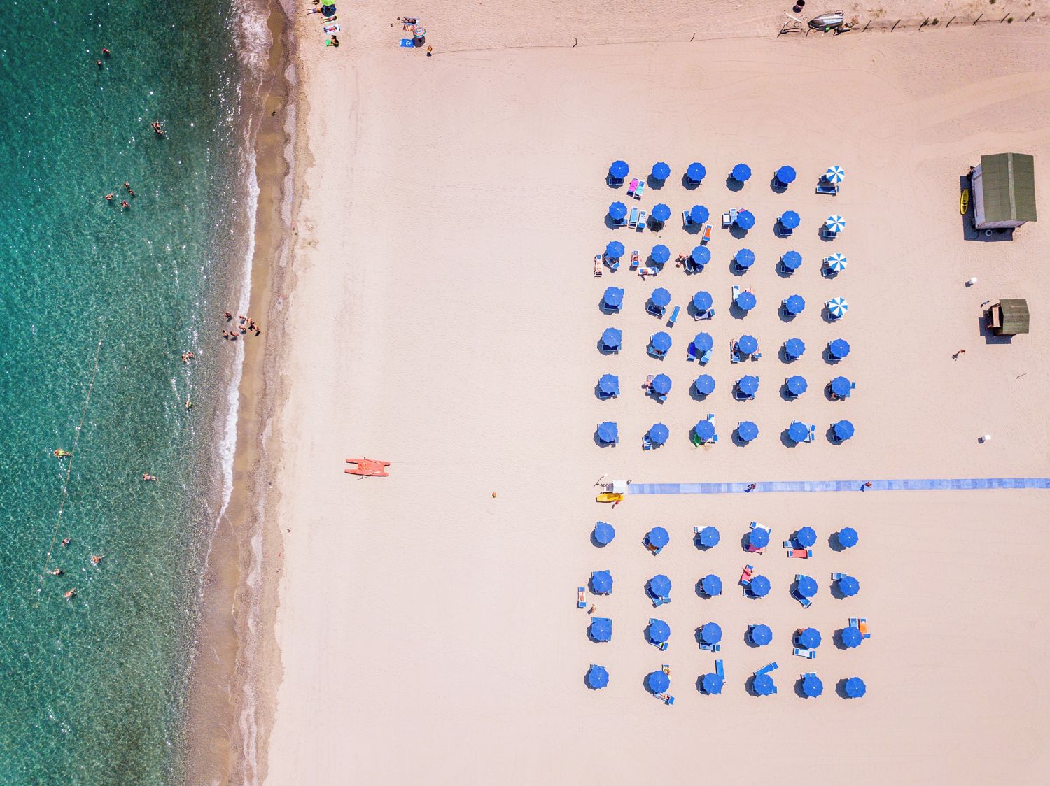 A beach with rows of blue umbrellas and beach chairs, a lifeguard tower, and a sandy shoreline.