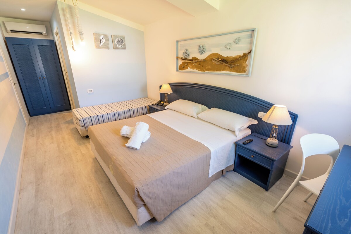 A hotel room with a bed, bedside tables, a chair, and artwork on the wall.