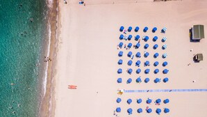 Una playa con hileras de sombrillas azules y sillas de playa, una orilla arenosa y agua turquesa cristalina.