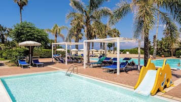 Una piscina cristallina con lettini e ombrelloni, circondata da palme.