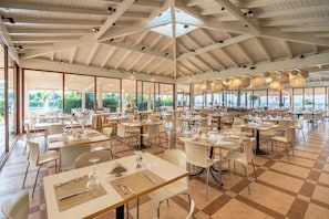 A spacious indoor dining area with multiple tables and chairs, large windows, and a high ceiling with exposed beams. - Le Dune Beach Club (Messina)