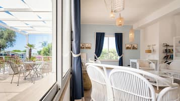 Una stanza con balcone, mobili in vimini bianco, un'ampia finestra con tende e un lampadario.
