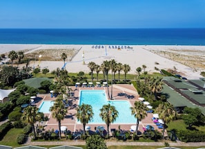 A resort with a large pool, beach access, and palm trees.