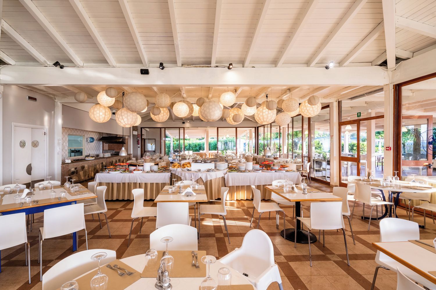 A spacious dining area with multiple tables and chairs, large windows, and hanging light fixtures.
