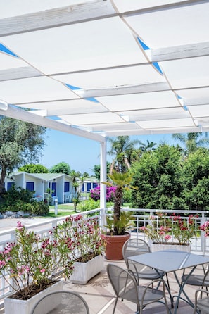 A covered outdoor area with a white pergola, potted plants, and outdoor furniture. - Le Dune Beach Club (Messina)