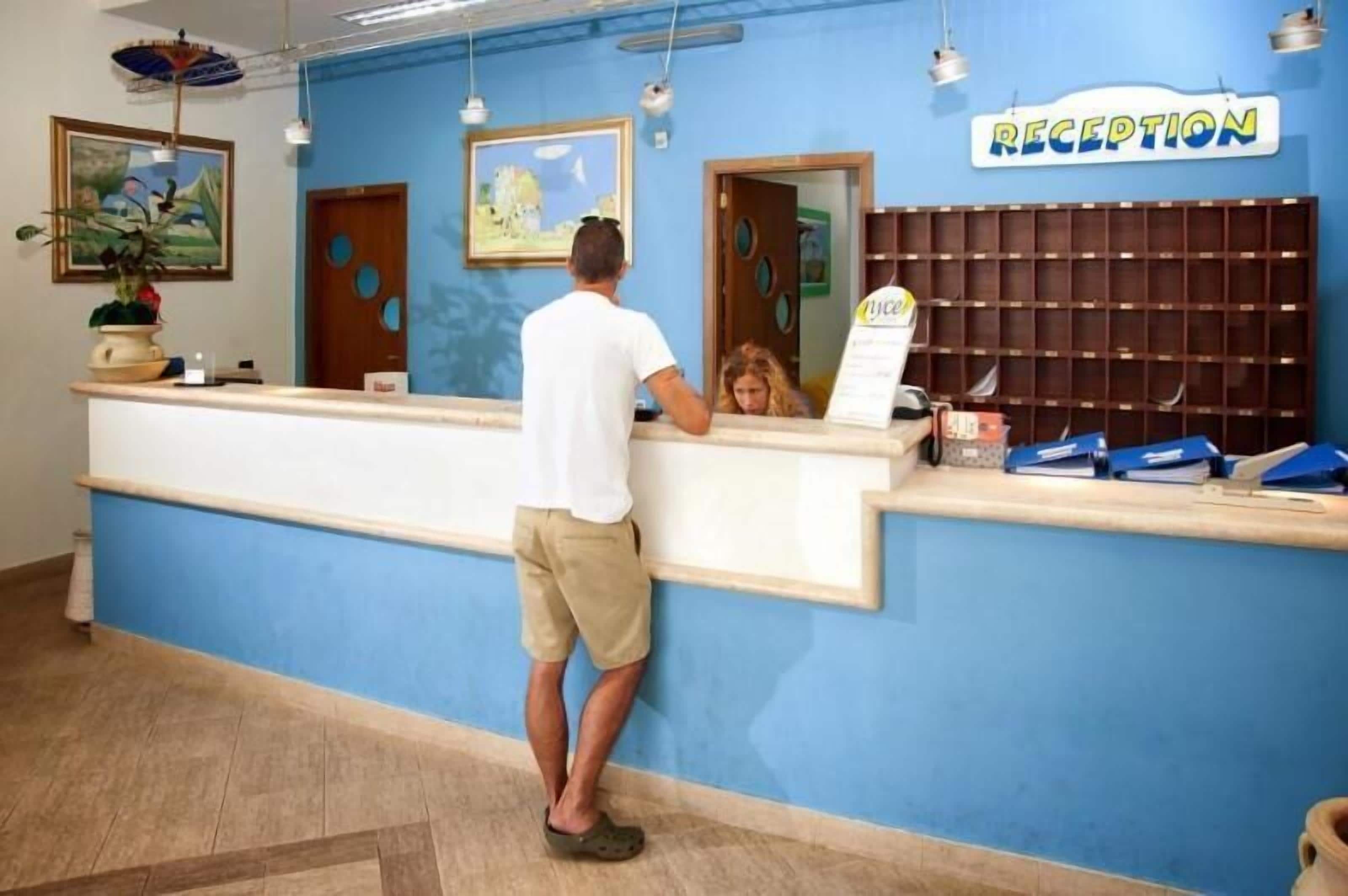 A reception desk with a blue wall, a 'RECEPTION' sign, and a man standing behind it.
