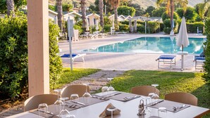 Comedor con mesa lista para seis personas, con vistas a una piscina y palmeras.