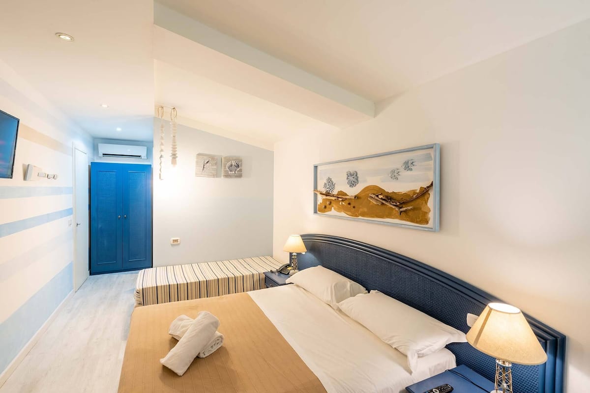 A hotel room with a bed, bedside tables, a blue door, and artwork on the wall.