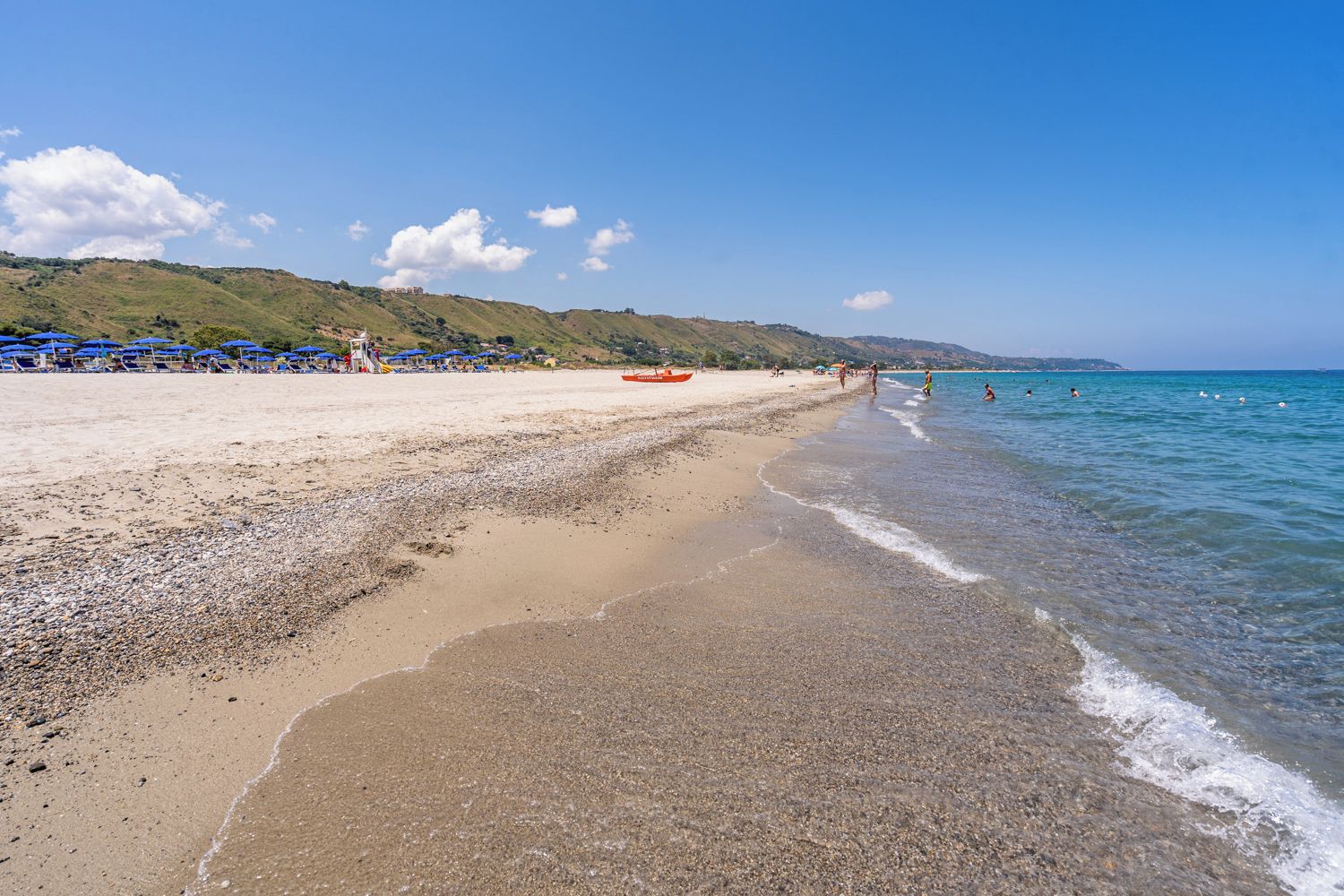 A beach with pebbles, a clear sky, and distant hills.