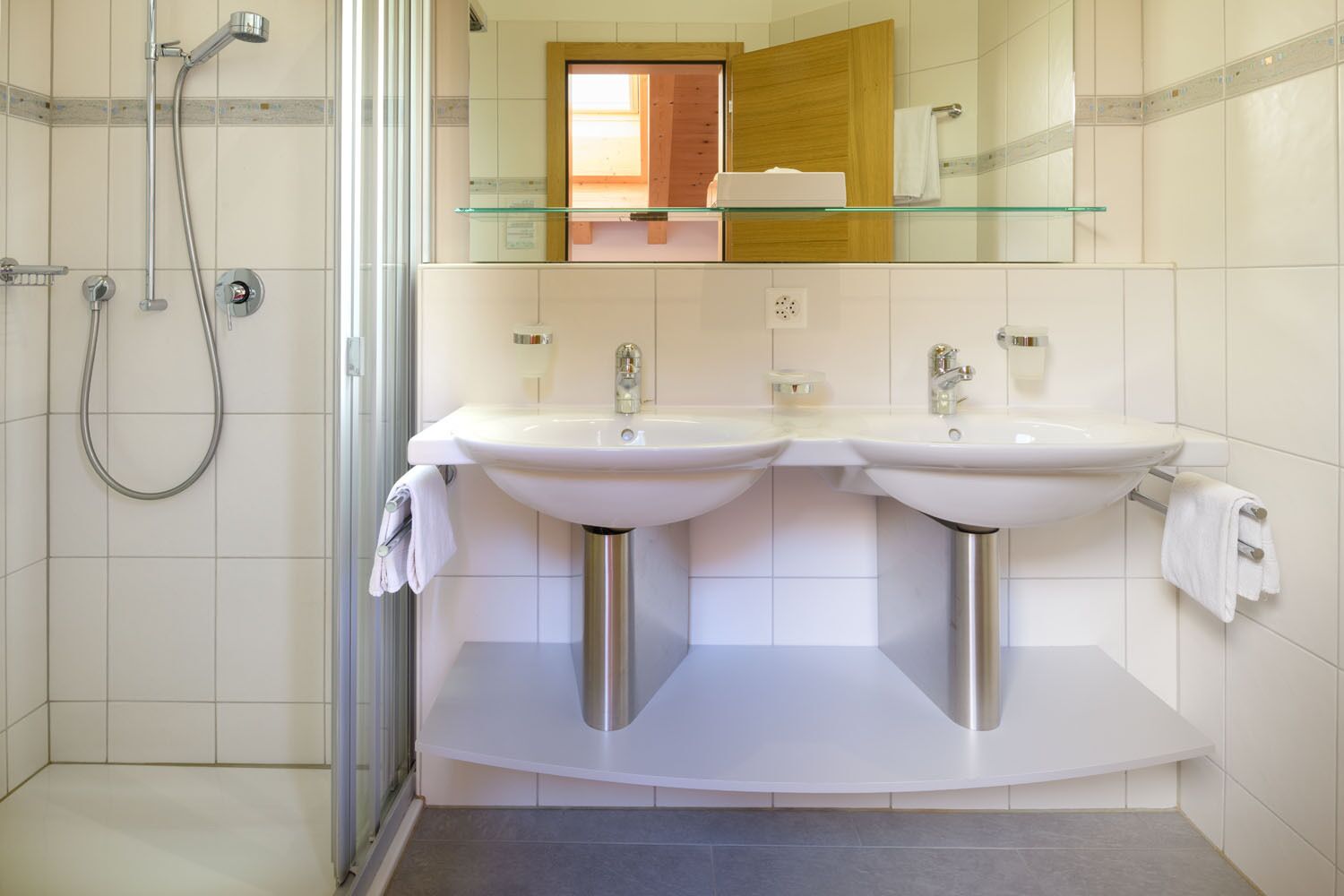 A modern bathroom with two sinks, a glass shower enclosure, and a mirror with a wooden frame.