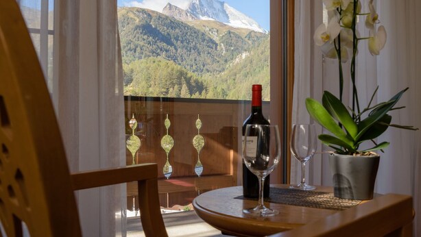 A balcony with a table, a bottle of wine, two wine glasses, and a potted plant. - Hotel Mountain Paradise (Zermatt)