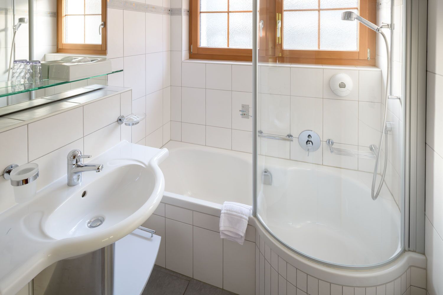 A modern bathroom with a white sink, glass shelf, and a glass-enclosed shower area.