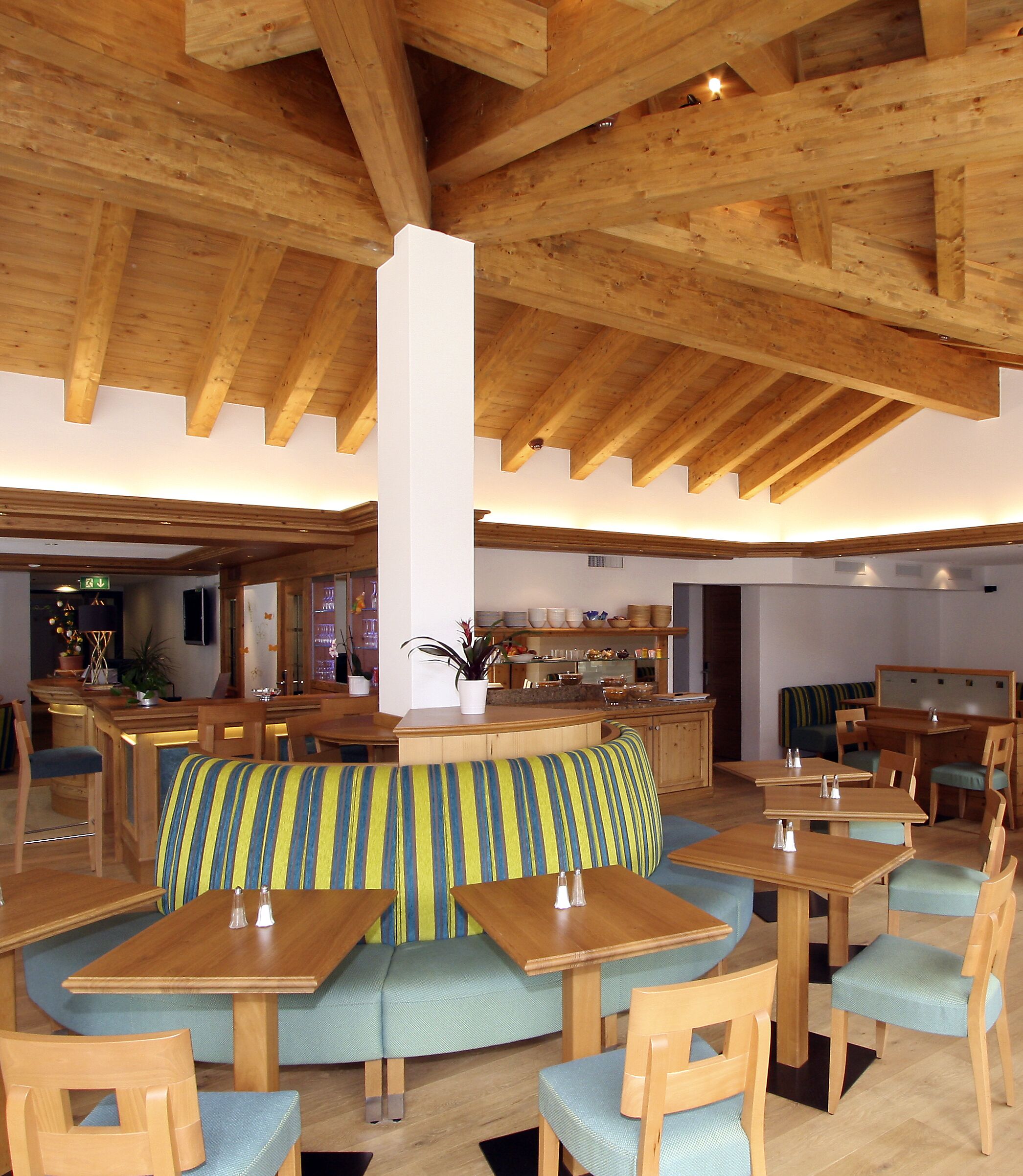 Un restaurante con vigas de madera, un área central de asientos con cojines a rayas y varias mesas y sillas.