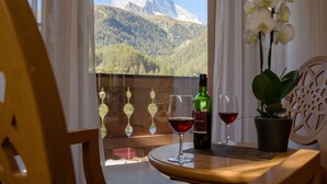 A balcony with a mountain view, a bottle of wine, two wine glasses, and a potted plant. - Hotel Mountain Paradise (Zermatt)
