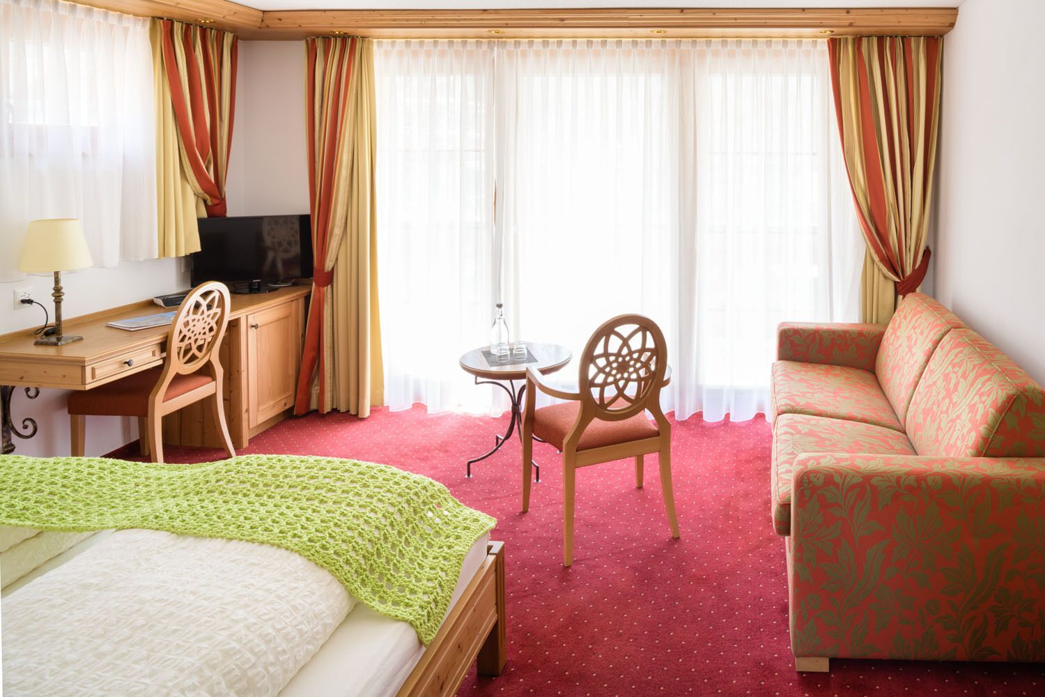 Une chambre d’hôtel comprenant un lit, un bureau avec un ordinateur, une télévision, une petite table avec des chaises et un canapé.