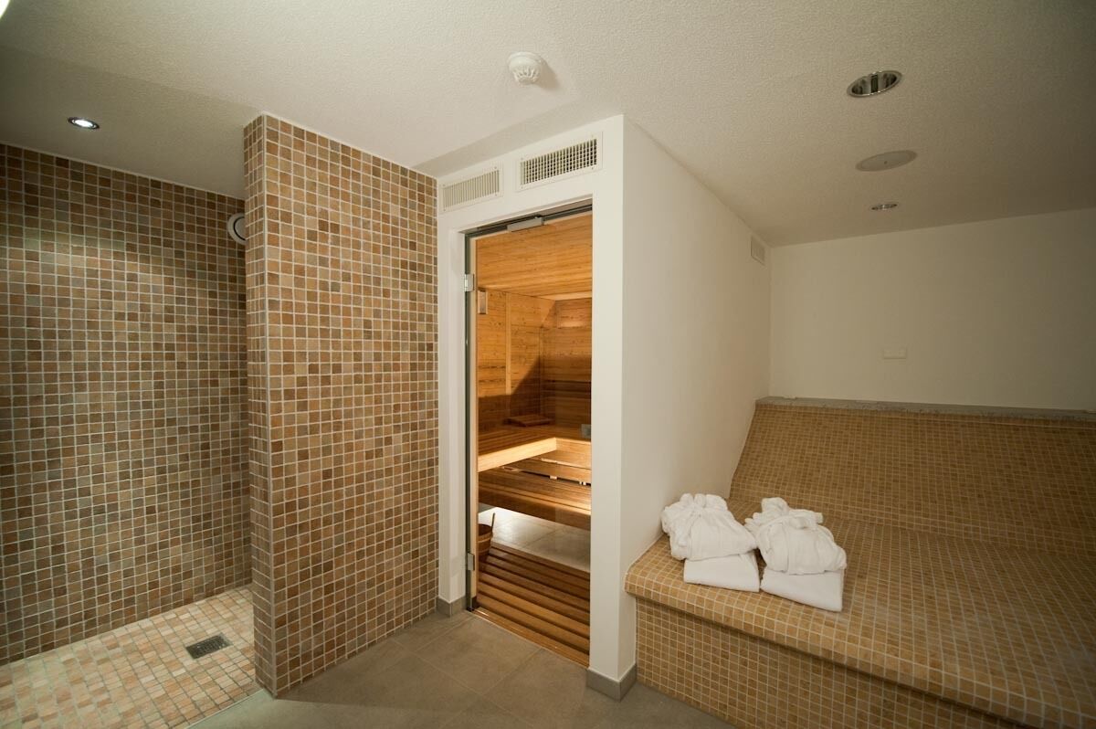 Une salle de spa dotée d’un sauna en bois, de murs carrelés et d’un banc avec des serviettes.