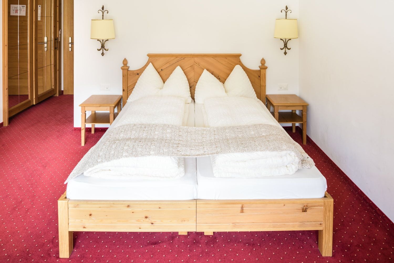Una cama doble con estructura de madera, dos mesitas de noche y lámparas fijadas a la pared.