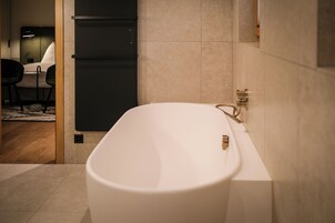 A modern bathroom with a freestanding bathtub, a wooden floor, and a small seating area with a table and chairs.