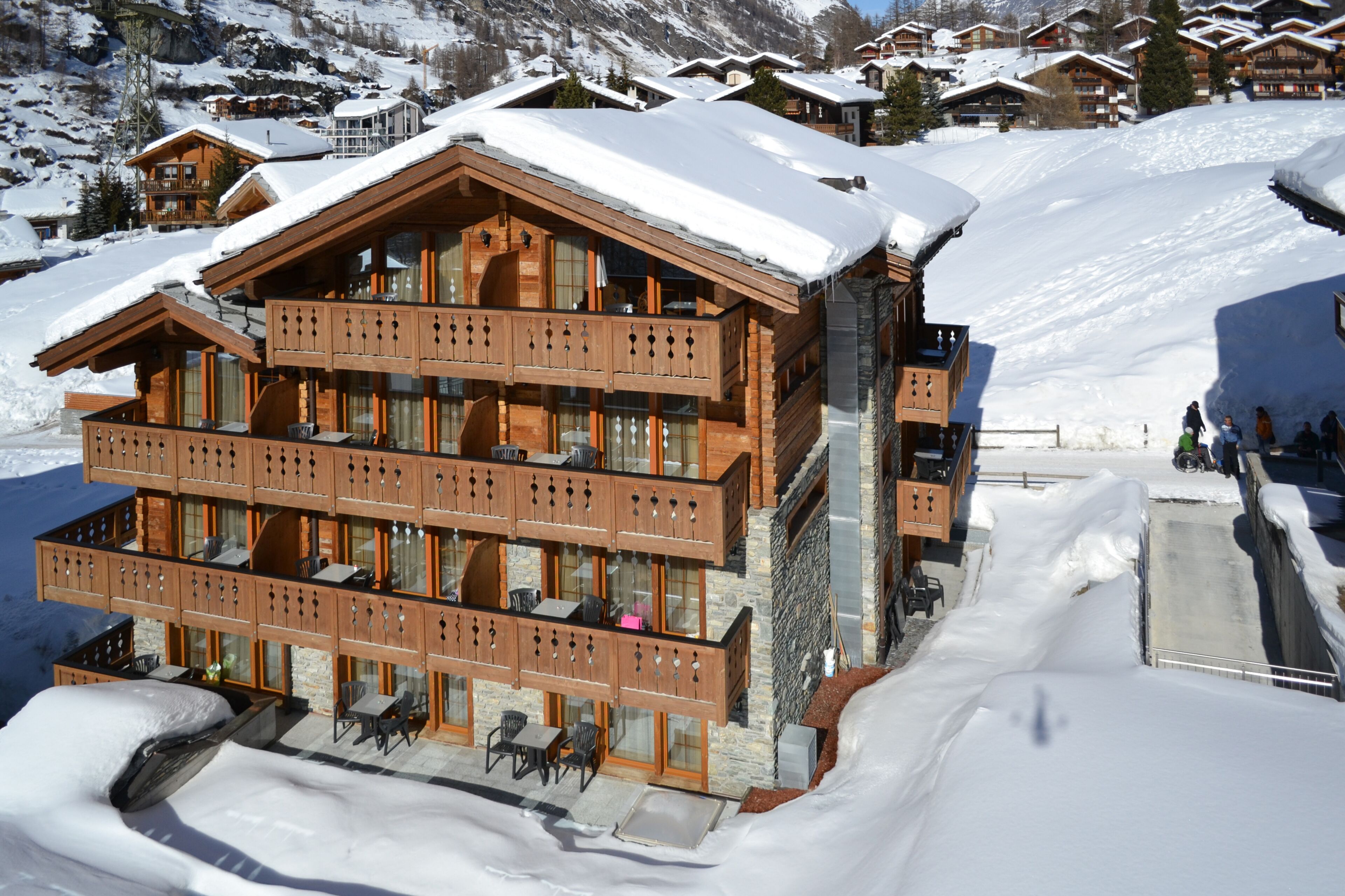 Un chalet de madera de varios pisos con balcones, una pista de esquí al fondo y paisajes nevados.
