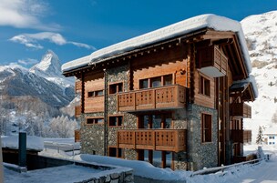 Un chalet de madera de varios pisos con paredes de piedra, balcones de madera y un techo cubierto de nieve.