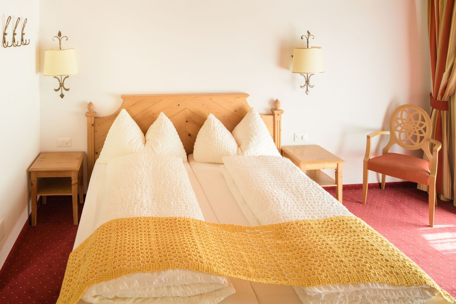 Ein Hotelzimmer mit einem hölzernen Bett, zwei Nachttischen, einem Sessel und Wandleuchten.