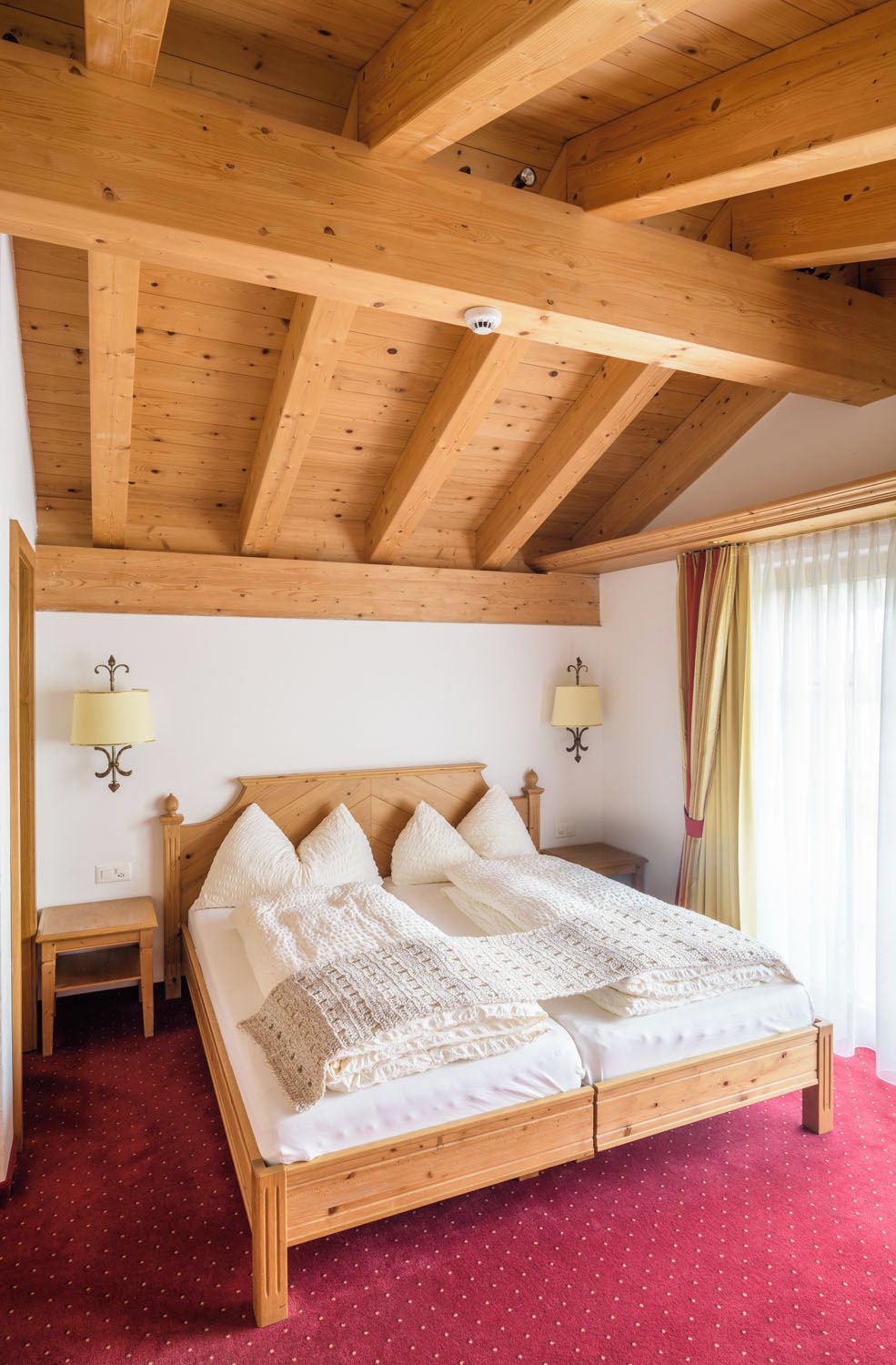 Un dormitorio con estructura de madera, una cama, dos lámparas fijadas a la pared y una alfombra roja.