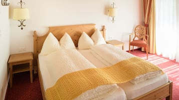 Habitación de hotel con cama de madera, ropa de cama blanca, manta amarilla, dos mesitas de noche, una silla y lámparas fijadas a la pared.