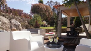 Un patio con mobiliario exterior blanco, una mesa redonda con bebidas y un muro de piedra al fondo.