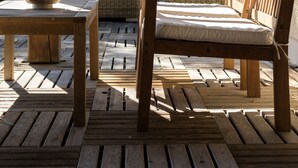 A wooden deck with a wicker sofa, a wooden chair, a table, and a hanging lantern.