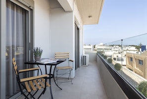 A balcony with a table and chairs, a potted plant, and a view of buildings.