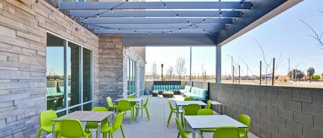Un patio exterior con mesas y sillas, una zona de estar cubierta y vistas del paisaje circundante.