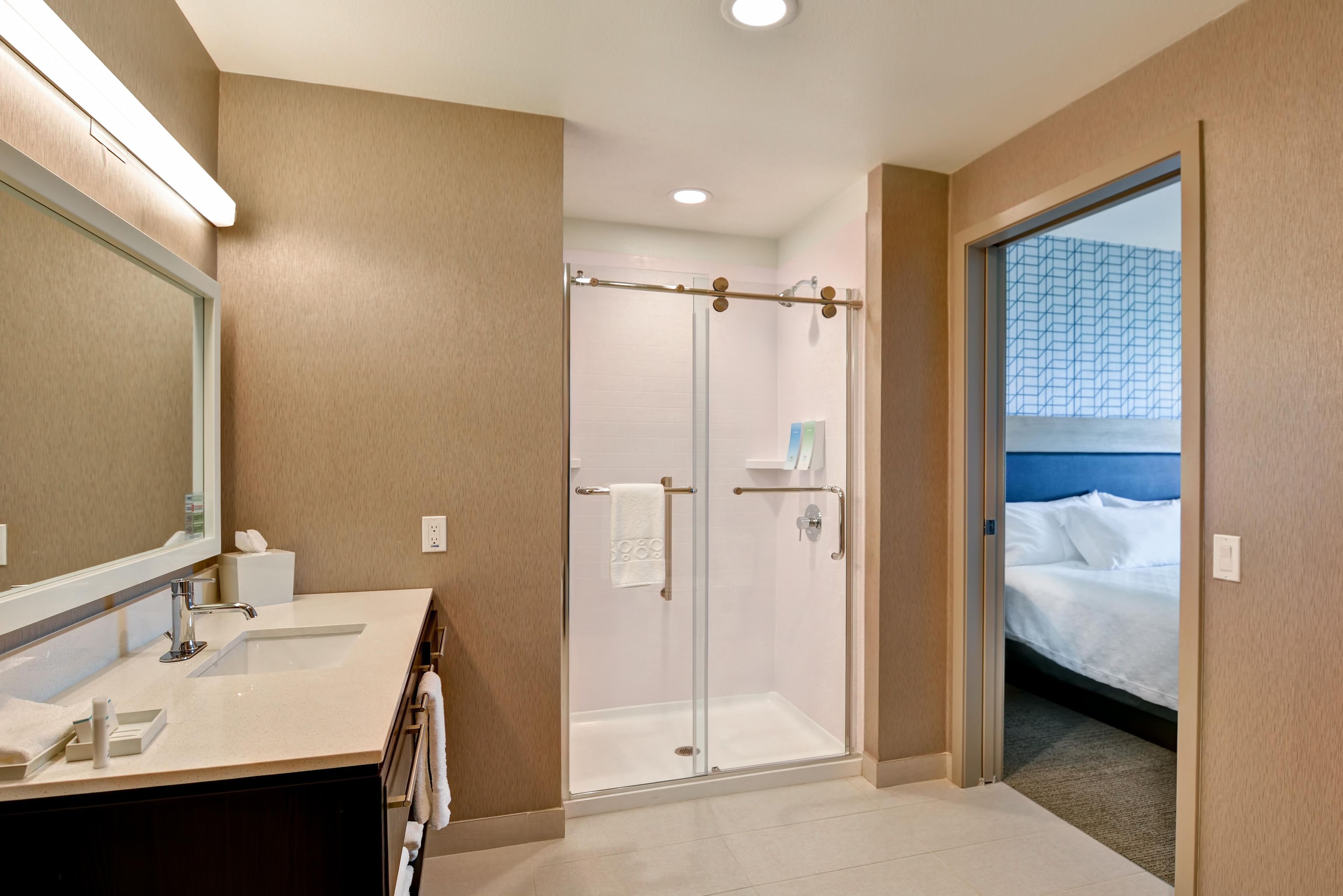 A hotel bathroom with a shower, a sink, and a mirror.