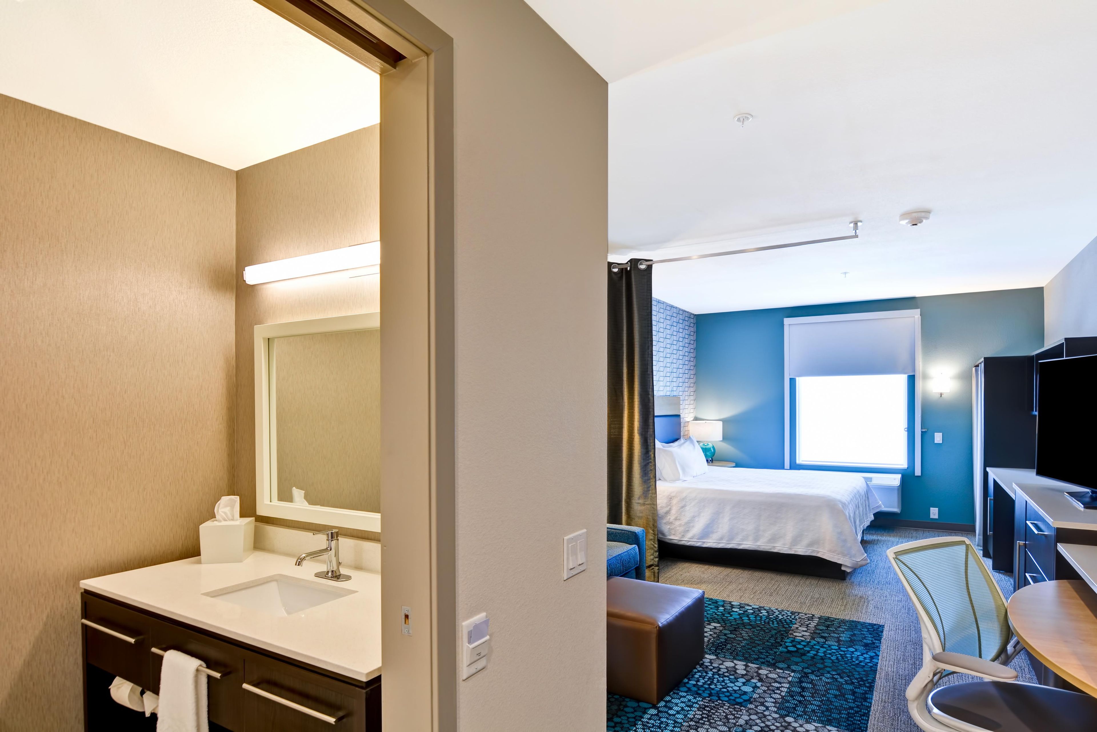 A hotel room with a bathroom, a bed, a desk, and a television.