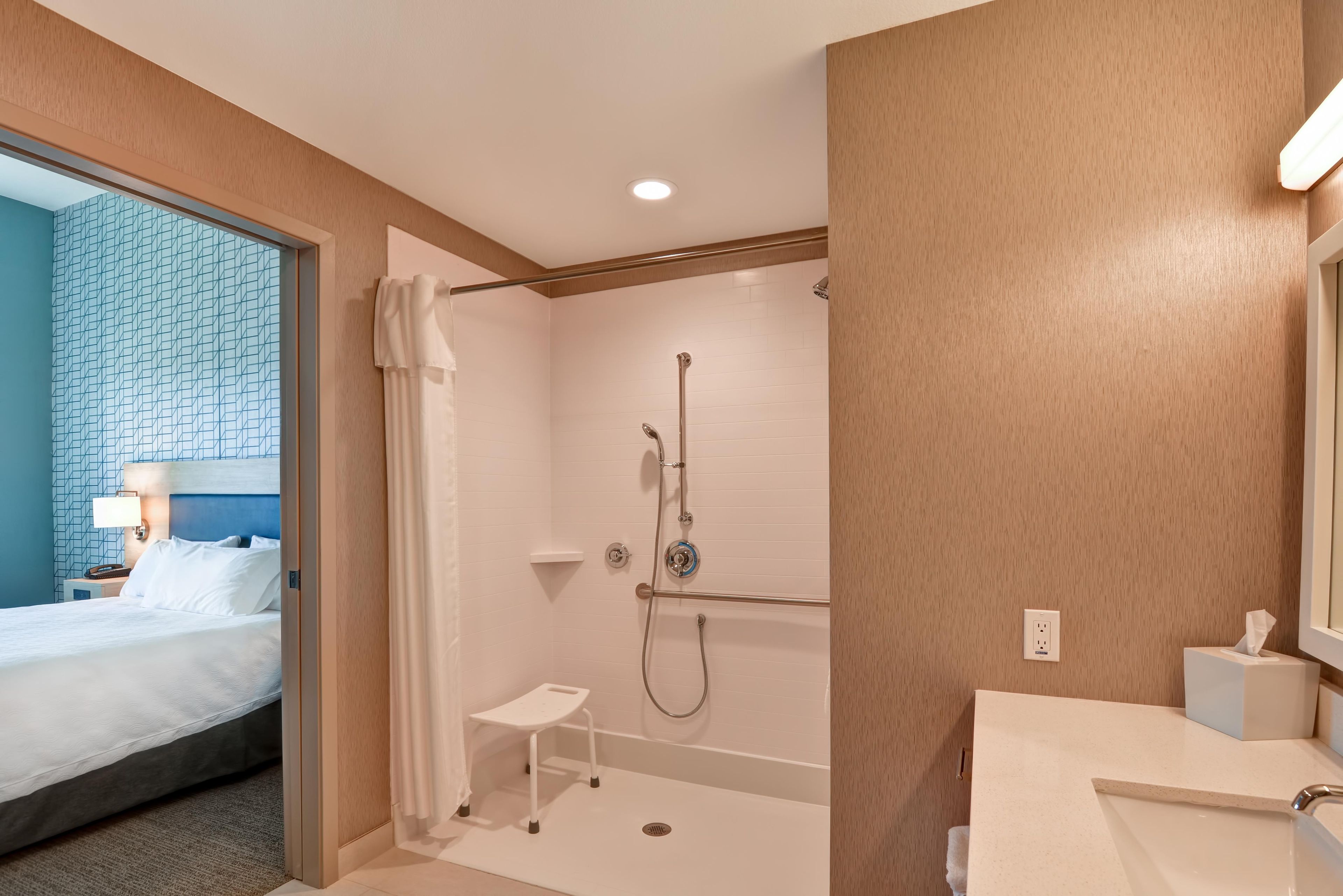 A hotel room with a bed, a shower, and a bathroom with a sink and mirror.