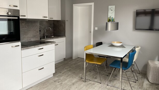 A modern kitchen with white cabinets, a black stove, and a dining area with a white table and two chairs.